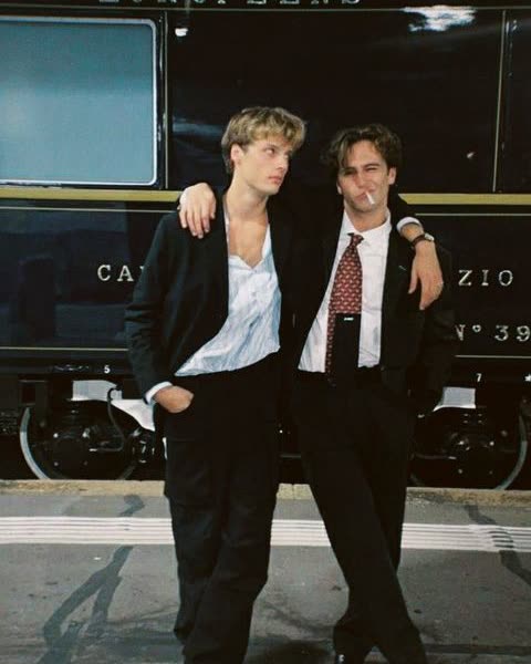 two boys in suits in front of a night train
