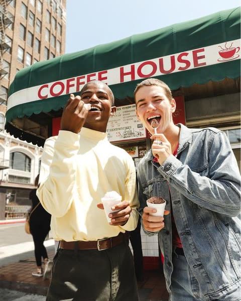 two friends laughing with coffees outside a coffee house